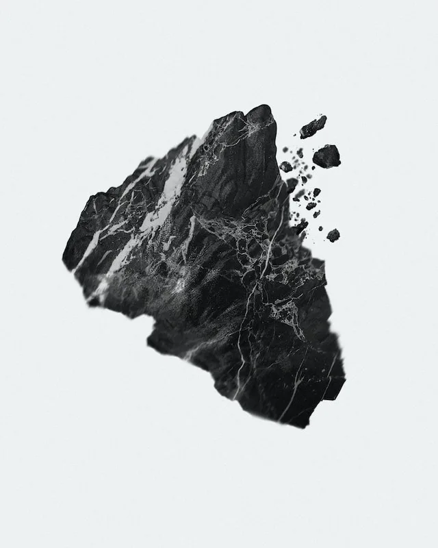 Black rock with white veining breaking apart into smaller fragments on a white background.